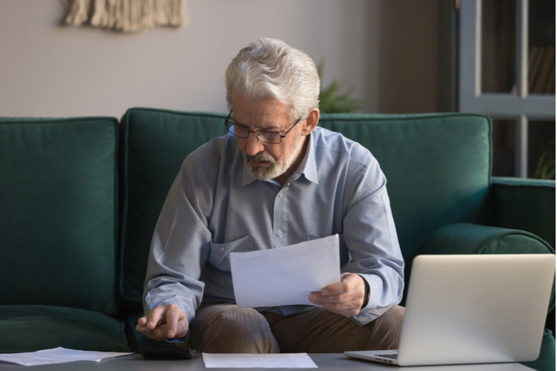 Elder man looks at calculator while holding papers
